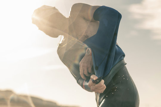 A swimmer in a wet suit on the beach, taking off one layer of clothing. 