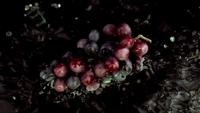grape falls on the wet table, black background, red grapes, slow motion