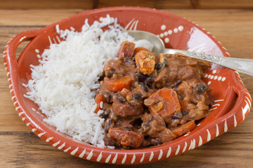 typical portuguese dish feijoada with rice in ceramic bowl on brown wooden background