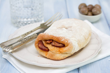 bread with chourico on white plate and glass of water on blue wooden background