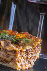 fresh hot steaming lasagna pasta served on wooden table and slate plate