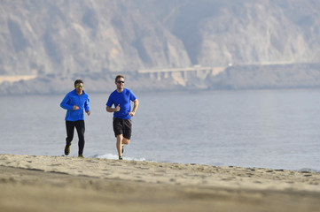 two men friends running together on beach sand coast mountain ba