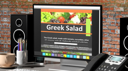 Monitor with Greek Salad recipe on desktop with office objects.