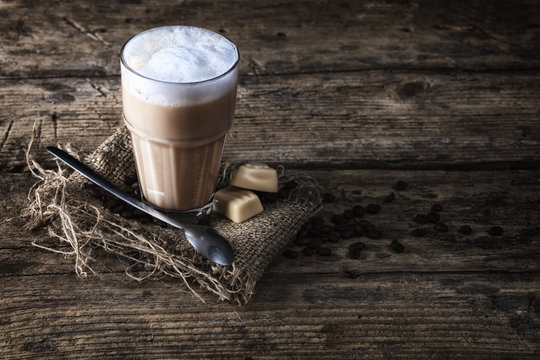 Milchkaffee mit Pralinen und Jute Unterlage auf einem Holztisch mit einem Kaffeelöffel