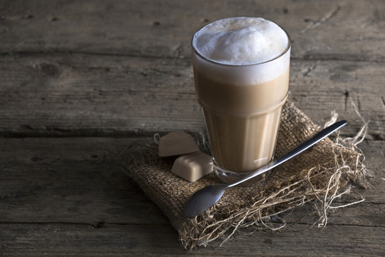 Milchkaffee mit Pralinen und Jute Unterlage auf einem Holztisch mit einem Kaffeelöffel