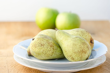Delicious green pears on white plate with apples on background