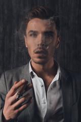 Fototapeta na wymiar Handome sexy man in suit on the grey background smoking a cigar