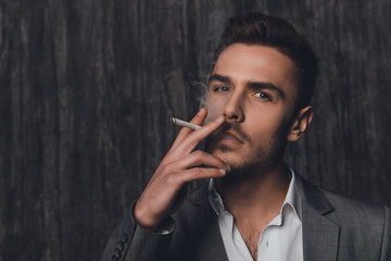 Portrait of a cheeky man in suit on the grey background smoking