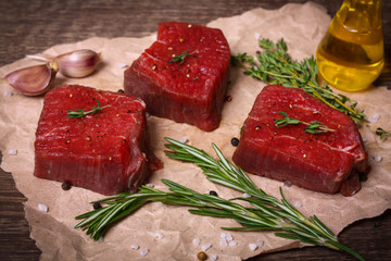 Raw beef steak with rosemary, thyme and garlic on wooden background