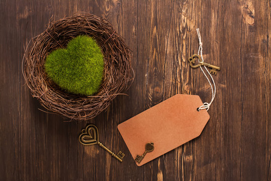 Green moss heart in a nest, keys and paper tag over wooden background. Valentines day concept. Toned image. Selective focus