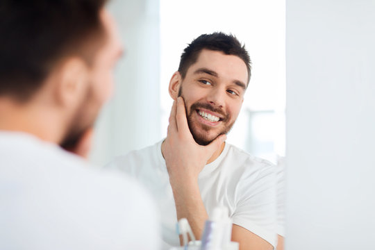 Happy Young Man Looking To Mirror At Home Bathroom