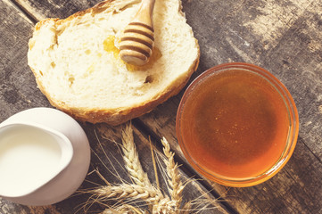 Honey in a jar, bread, wheat and milk on wood table.