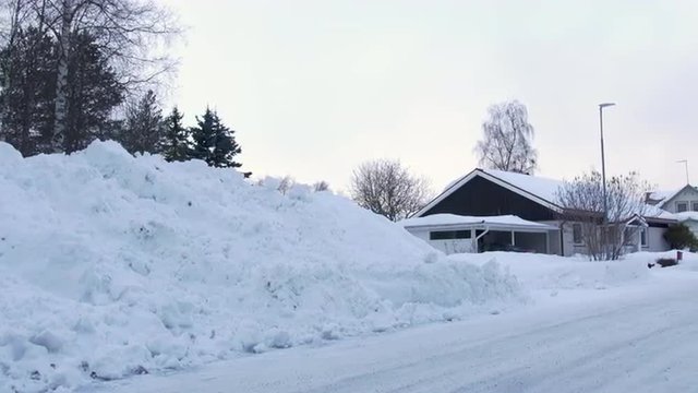 Pan of a very snowy street in a suburban area. Starts with a big pile of snow and pans so the viewer can see the street. Filmed in 4k (UHD Ultra HD 3840x2160 resolution. 2160p.

