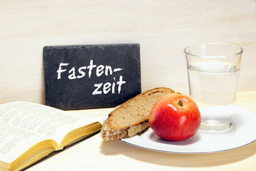 Fastenzeit - Tafel mit Schrift, Gebetbuch, Brot, Apfel, Glas Wasser