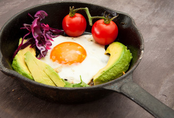 Breakfast skillet pan of fried egg, avocado and tomato. Served on a gray stone slate background.