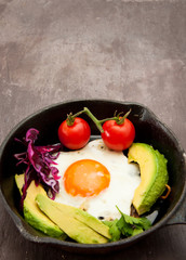 Breakfast skillet pan of fried egg, avocado and tomato. Served on a gray stone slate background.