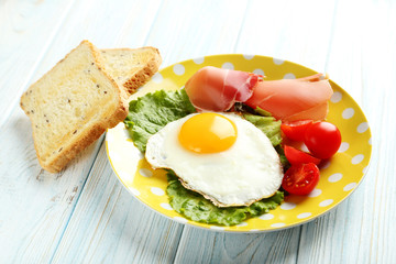 Fried eggs with bacon and toasts on plate on blue wooden table
