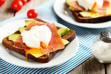 Poached eggs with avocado and bacon on toasts on grey wooden tab