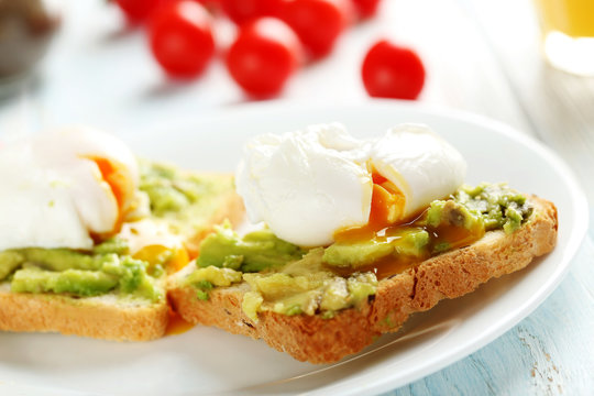 Poached eggs with avocado on toasts on blue wooden table