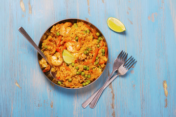 Traditional spanish paella dish with seafood, peas, rice and chicken over grunge blue background. Top view. Selective focus