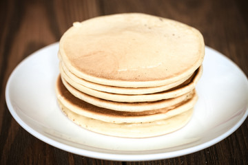stack of pancakes on a white plate, brown background of wooden p