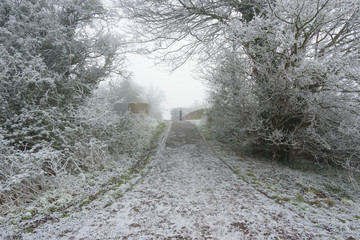 A frost covered footpath going over a canal bridge on a cold and foggy winters day.