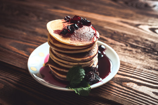 stack of pancakes on a white plate with cherry jam, mint leaves,