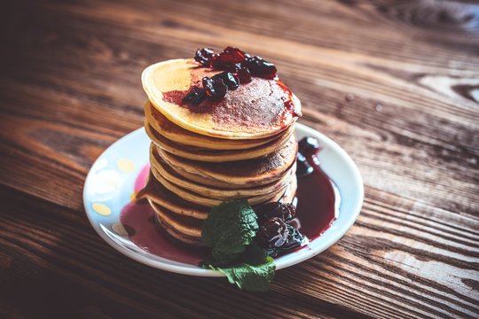 stack of pancakes on a white plate with cherry jam, mint leaves,