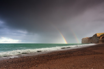 rainbow over sea waves by rock after shower