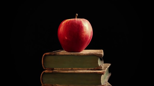 Apple of knowledge. Red apple on book stack. Camera movement right to left.