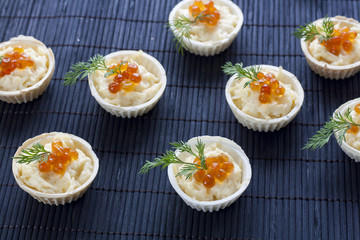 Tartlets with cream cheese and red caviar close up on the black background.