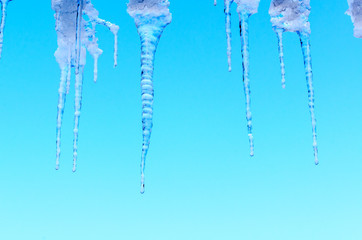 Spring thaw, ice icicles on blue sky background.