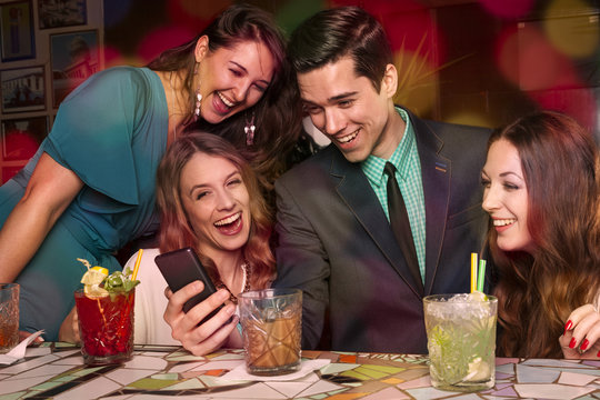 Vier Freunde sehen sich zusammen Urlaubsbilder auf dem Smartphon