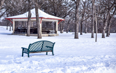 Park bench in winter park with snow and pavilion 