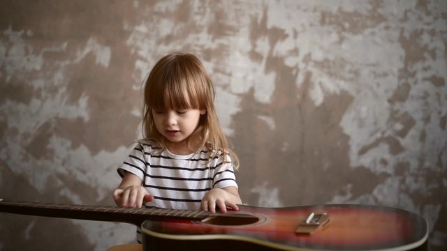 Little girl is playing with a guitar on a grunge background. Soft focus. Vignette is added.