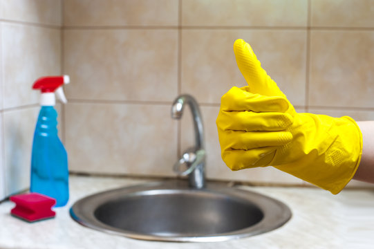Hand in yellow glove showing thumb up on the background of sink. Finished cleaning. Cleaning concept.