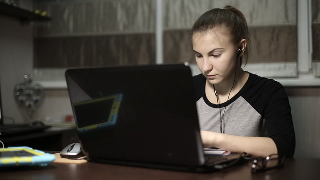 
Young business ladies working at a laptop with headphones at night