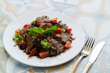 Warm salad with beef, tomatoes and lettuce on a white plate