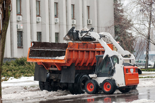 loader pours the snow into the truck on the street