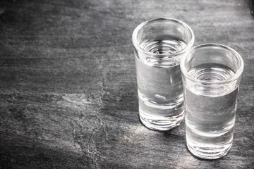 Two vodka shots on black grunge surface.