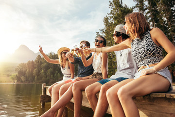 Young friends sitting on a pier toasting beers