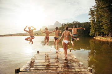 Young friends jumping into a lake - obrazy, fototapety, plakaty
