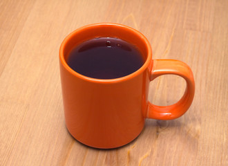 Orange cup from ceramics with tea on brown wooden table closeup