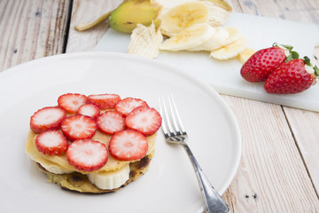 Stack of golden pancakes with strawberries, banana,