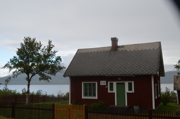 Fototapeta na wymiar Red wooden Scandinavian house at a lakeside, Torneträsk, Abisko, Swedish Lapland