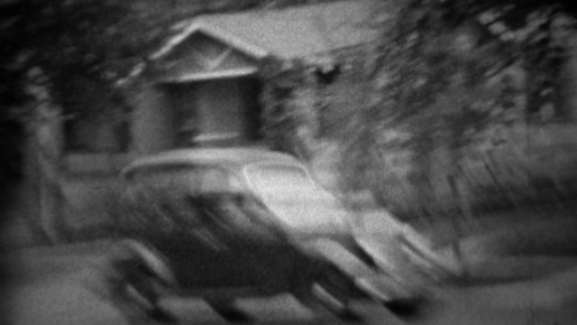1935: Classic new black Plymouth car driving residential neighborhood.