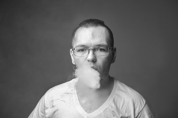 Black & white portrait of hip young man wearing eye glasses and white tee shirt blowing out smoke