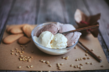 vanilla, chocolate, berry ice cream in a bowl with a spoon on a wooden table with nuts and biscuits
