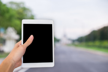 Hands are holding touch screen White Tablet Computer on the ways blurred background.