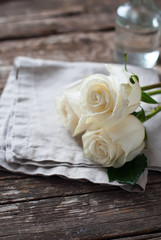 Three White Roses on linen napkin and Wooden Table. Vintage